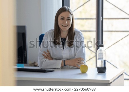 Female nutritionist smiles at camera and shows an apple and a water bottle. Healthy eating concept
