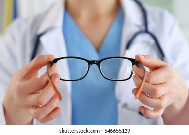 Female oculist doctor hands giving pair of black glasses to patient. Eyesight correction. Ophthalmology, excellent vision or optician shop concept. Laser surgery alternative.