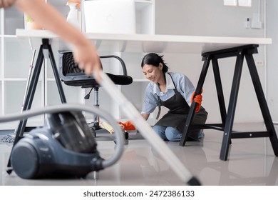 Female office cleaner wiping floor under desk with vacuum in foreground. Concept of thorough workplace cleaning - Powered by Shutterstock