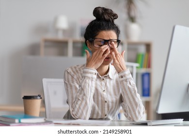 Female office worker in glasses rubbing tired eyes, exhausted from overworking, sitting at workplace in office, copy space. Young businesswoman feeling eye fatigue or pain - Shutterstock ID 2149258901