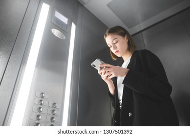 Female office worker is looking at her smartphone screen in the elevator. Businesswoman checking messages on her cellphone in the lift. Copyspace. - Powered by Shutterstock