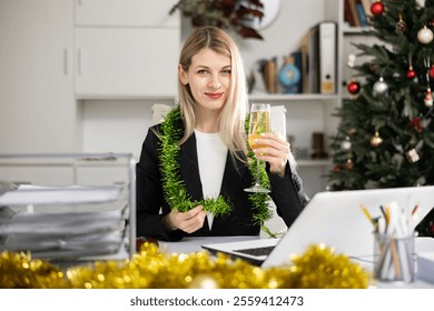 Female office worker sitting in her workplace among Christmas decorations with glass of champagne, smiling and looking at camera. - Powered by Shutterstock