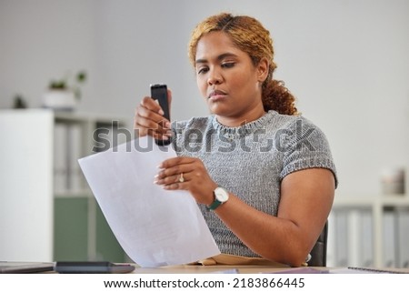 Female office worker stapling paper together in her office at work, being efficient, organized and neat. Young female admin clerk sorting and filing paperwork while sitting and working at her desk