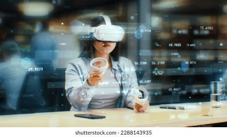 Female office worker uses VR headset and wireless controllers, watches data and numbers in 3D virtual reality. Asian woman works in modern hi-tech IT company. Future innovative digital technologies. - Powered by Shutterstock