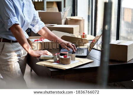 Female online store small business owner entrepreneur seller packing shipping ecommerce box checking website retail order using laptop preparing delivery parcel on table. Dropshipping concept. Closeup