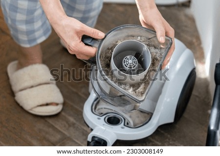 Female opening dust filter out of vacuum cleaner at home. Hoover container full of dirt, fur, pet hair after cleaning at home. Dust in apartment is source of allergies. Household chores concept