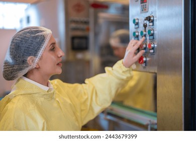 A female operator in a cleanroom suit attentively adjusts the control panel of a beverage bottling machine in a modern manufacturing plant. - Powered by Shutterstock