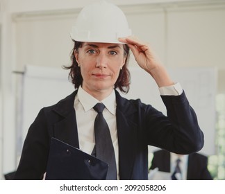 Female Operator Managing Director In Manufacturing Wears Black Suit And White Safety Helmet Ready To Work. Portrait Of Beautiful Middle Aged Professional Executive Woman Busy Working Looking At Camera