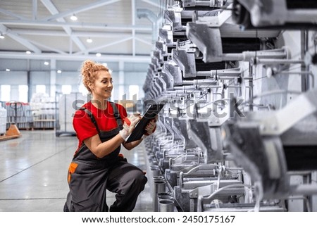 Female operator working taking notes of production line machine inside factory.