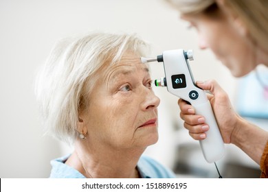 Female ophthalmologist measuring the eye pressure with modern tonometer to a senior patient in the medical office, close-up view