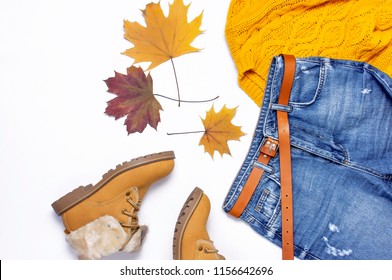 Female orange knitted sweater, blue jeans, boots and autumn leaves on white background top view flat lay. Fashion Lady Clothes Set Trendy Cozy Knit Jumper Autumn accessories Female fashion look