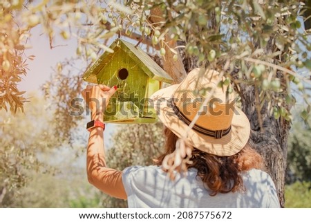 Female ornithologist and birdwatcher pours food into a birdhouse hanging on an olive tree in the park. Hobby and leisure concept