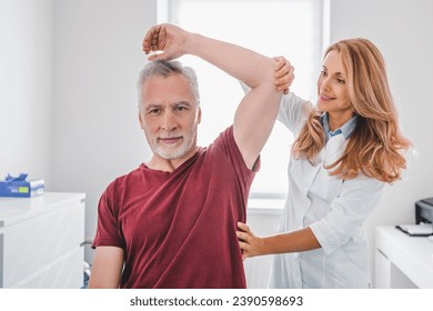 Female orthopedist examining patient in hospital. Reflexology, injuries in joints and muscles treatment. Caregiver helping to stretch arms for elderly patient - Powered by Shutterstock