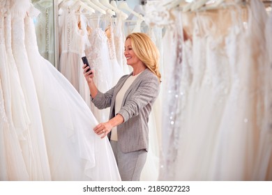 Female Owner Of Bridal Wedding Dress Shop Taking Photo On Mobile Phone