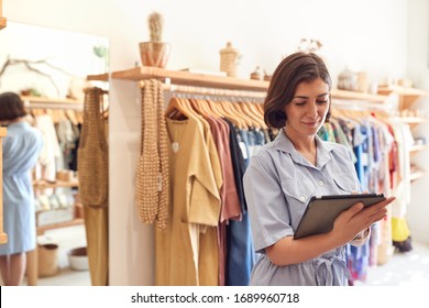 Female Owner Of Fashion Store Using Digital Tablet To Check Stock On Rails In Clothing Store