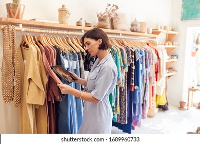 Female Owner Of Fashion Store Using Digital Tablet To Check Stock On Rails In Clothing Store