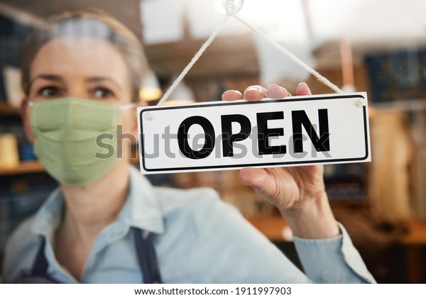 Female Owner Of Small Business\
Wearing Face Mask Turning Round Open Sign During Health\
Pandemic