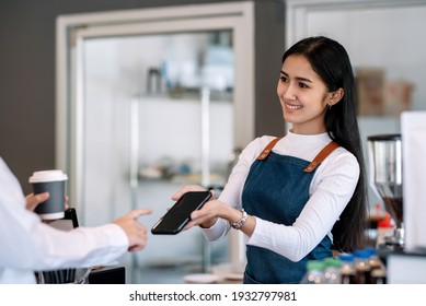 Female Owner Of A Small Coffee Shop. Customer Pay For Food Through Their Mobile Phone At The Coffee Shop.