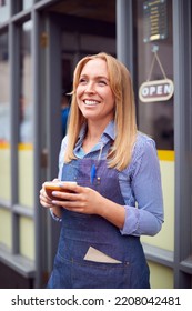 Female Owner Or Staff Standing Outside Coffee Shop Holding Hot Drink