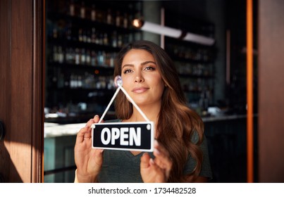 Female Owner Of Start Up Coffee Shop Or Restaurant Turning Round Open Sign On Door