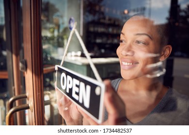 Female Owner Of Start Up Coffee Shop Or Restaurant Turning Round Open Sign On Door