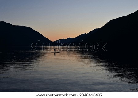 Female paddleboarder in silhouette at sunset on Lake Crescent in Olympic National Park, Washington on calm clear summer afternoon.