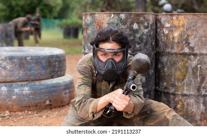 Female Paintball Player In Camouflage And Mask Aiming With Gun In Shootout Outdoors