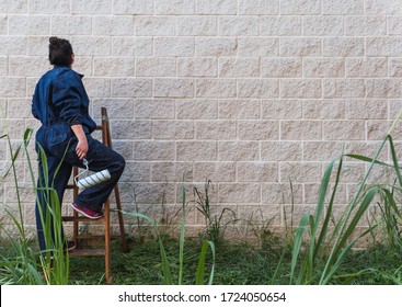 Female Painter Climbing The Ladder In Front Of A Concrete Block Wall