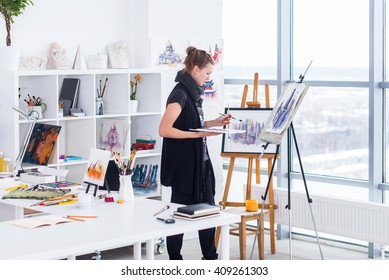 Female painter drawing in art studio using easel. Portrait of a young woman painting with aquarelle paints on white canvas, side view portrait - Powered by Shutterstock