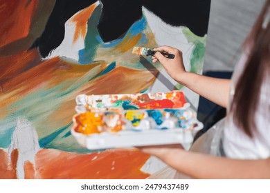 Female painter hand passionately paints picture with paintbrush for outdoor street exhibition using vibrant colors, close up view - Powered by Shutterstock