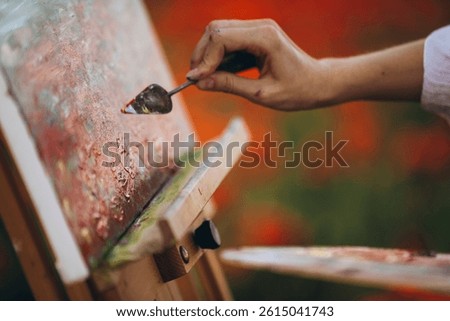 Female painter using spatula while painting in a poppy field, adding a touch of red to her artwork