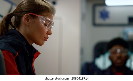 Female Paramedic Using Mobile Phone In Emergency Car. Portrait Tired Ambulance Doctor Discussing Work With Colleague. Emergency Medical Technician Going On Car Accident. Healthcare Concept