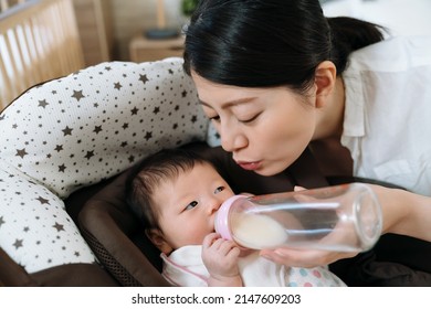 female parent is pursing her lips and making playful sound while whatching her child drinking milk. pleasant atmosphere chinese mom playing kiss with her baby while feeding with the aid of a bouncer