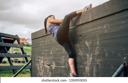 Female Participant In An Obstacle Course Climbing A Wall