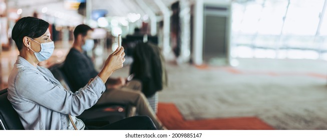 Female Passenger Doing Video Call While Sitting At Airport In Pandemic. Woman With Facemask Waiting At Airport And Video Calling.