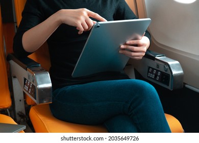 Female Passenger Reading And Working On Computer Tablet In Airplane Window Side Seat