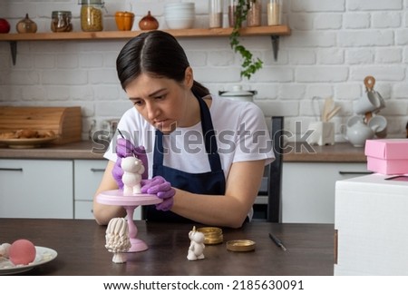 Female pastry chef covers chocolate bear figurine with gold with brush. Selective focus. Image for articles about confectionery.