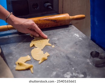 Female pastry chef skillfully uses star-shaped cookie cutter to create delightful cookies from cookie dough on gray kitchen counter. Nearby, wooden rolling pin rests, creations and delicious treats. - Powered by Shutterstock