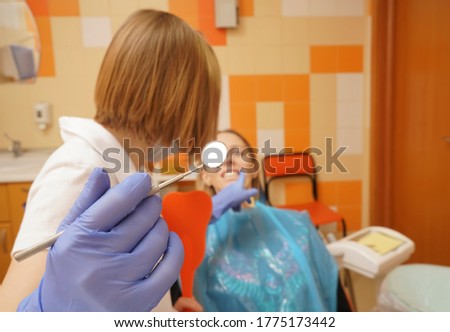 female patient being examined by dentist, wearing in latex gloves, in clinic.Young caucasian woman, sitting in chair of dentist, looking straight with open mouth while doctor checking teeth