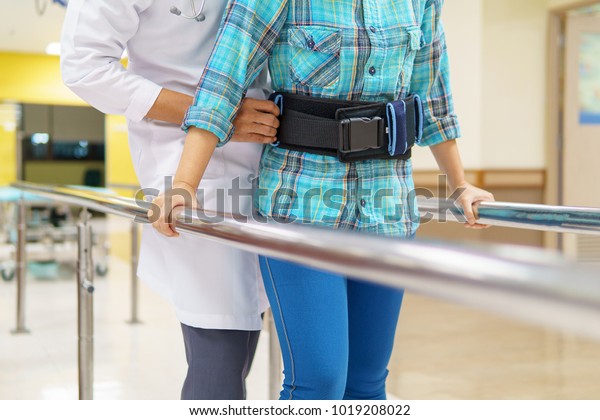 Female patient\
with a doctor holding a belt to support the walk with the Parallel\
Bar can be used to hold the support for stability while walking.\
medical and healthcare\
concept.