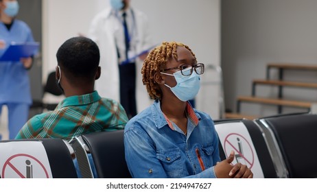 Female Patient With Face Mask Sitting In Waiting Room Area, Having Consultation Appointment With Specialist At Hospital Reception. Woman Attending Checkup Visit During Covid 19 Pandemic.