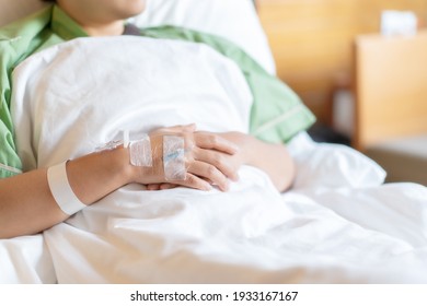 Female Patient In A Green Hospital Gown Lies On A Bed With Heparin Lock For Intravenous Drug Use. Medical And Health Care