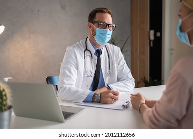 Female Patient Is Having An Appointment At Doctor. They Are Sitting In His Office And Speaking While Wearing Medical Masks