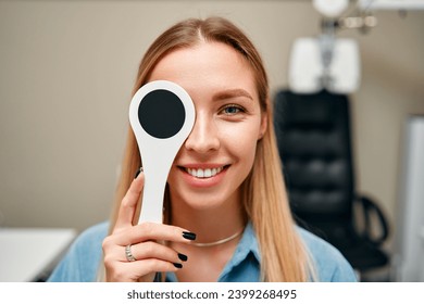 A female patient is having her eyesight checked in an ophthalmology clinic with one eye closed. Ophthalmology and vision testing concept.
