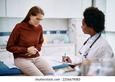 Female patient holding her abdomen in pain while talking to her doctor at medica clinic.
