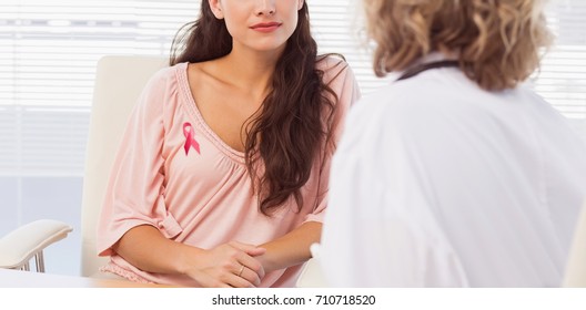 Female patient listening to doctor with concentration in medical office against breast cancer ribbon