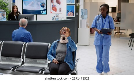 Female Patient With Neck Collar Brace Attending Checkup With Doctor And Nurse, Receiving Medical Treatment And Care After Accident Injury. Woman Wearing Cervical Foam In Hospital Reception Lobby.