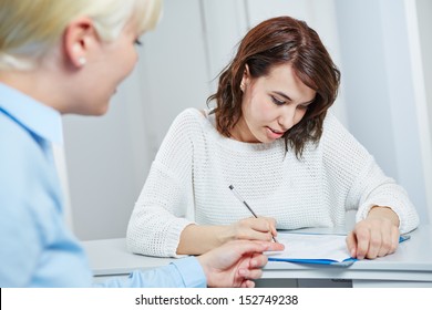 Female Patient At Reception Of Doctors Office Filling Out Medical Form