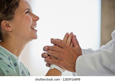 Female Patient Smiling As A Doctor Holds Her Hands And Tells Her Good News.