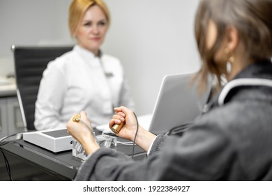Female patient takes hold of the brass handpieces of bioenergetic testing device in medical clinic with doctor on background. Health and wellness concept.